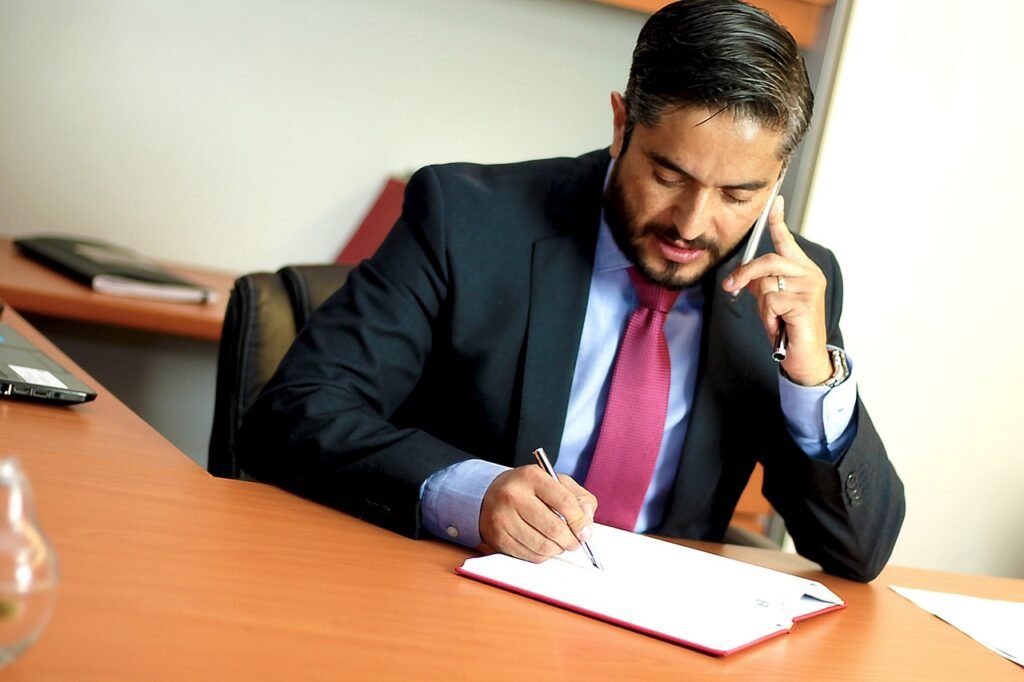 a man in a suit talking on the phone while writing on a notebook